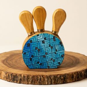Base de madera de $10 \times 9\text{ cm}$ equipada con 3 cuchillos para queso de acero con mangos de madera. La cara frontal está meticulosamente pintada a mano por artesanos de Oaxaca utilizando técnicas tradicionales de alebrije en patrones geométricos azules y negros. Una vajilla artesanal de alta gama ideal para tablas de carnes frías, reuniones gourmet o como un regalo corporativo y cultural exclusivo.