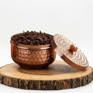 Especiero redondo de cobre martillado hecho a mano con tapa sobre una base de madera rústica.