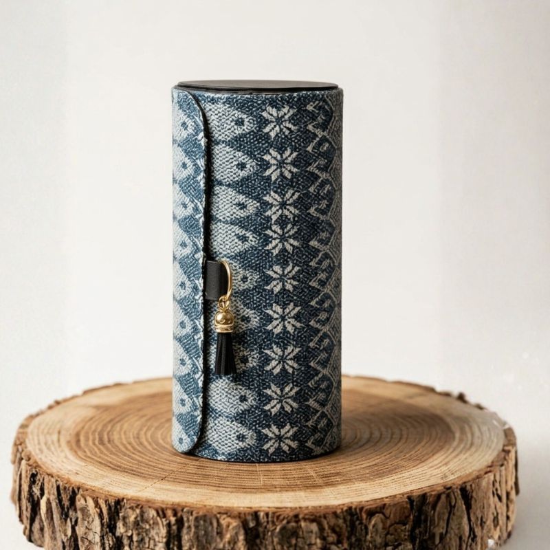 Alhajero cilíndrico forrado con textil de rebozo tradicional azul y blanco sobre una base de madera rústica.